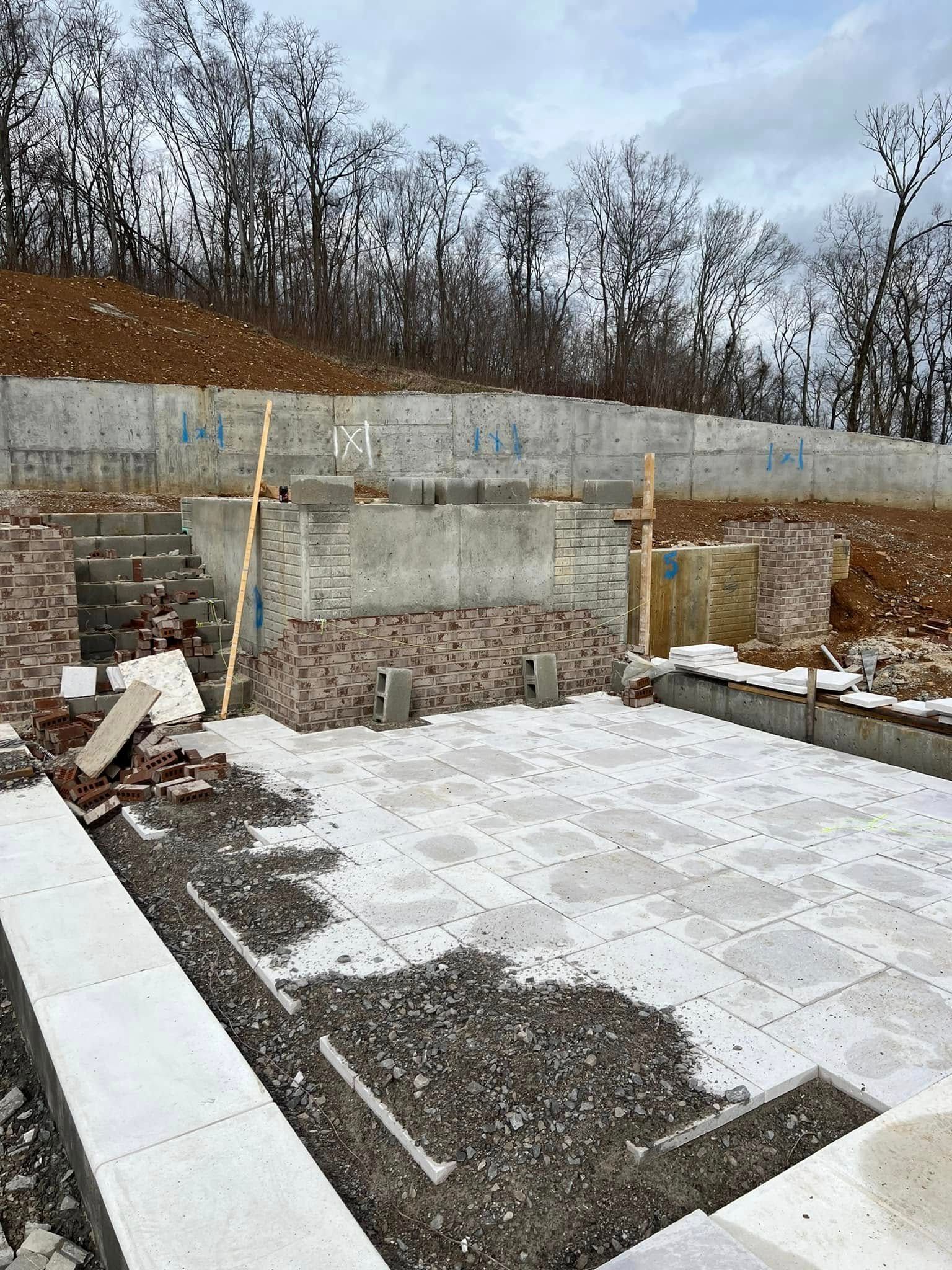 Stone retaining wall and stepped gravel construction site with wooden supports and bare trees in the background