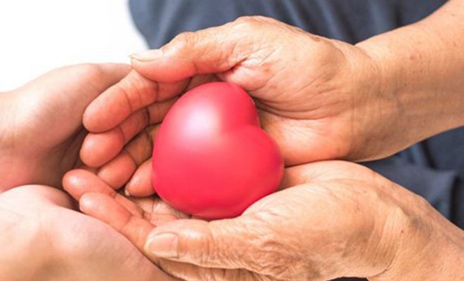 Two hands, one younger and one older, holding a red heart together