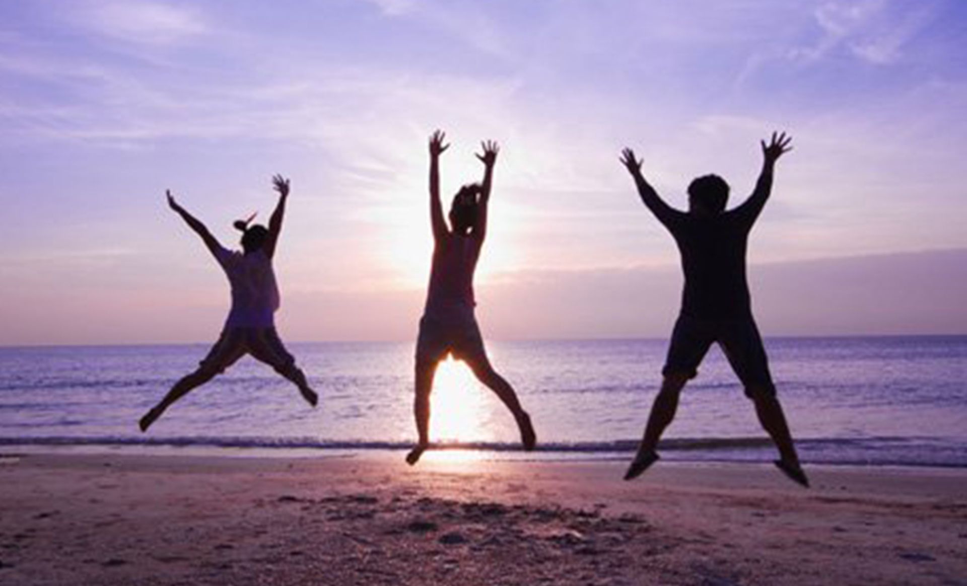 Three silhouetted people jumping on a beach with the sun setting