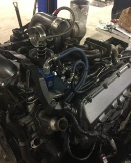 Turbocharged engine with blue hoses, silver turbo, and black components, in a shop setting.