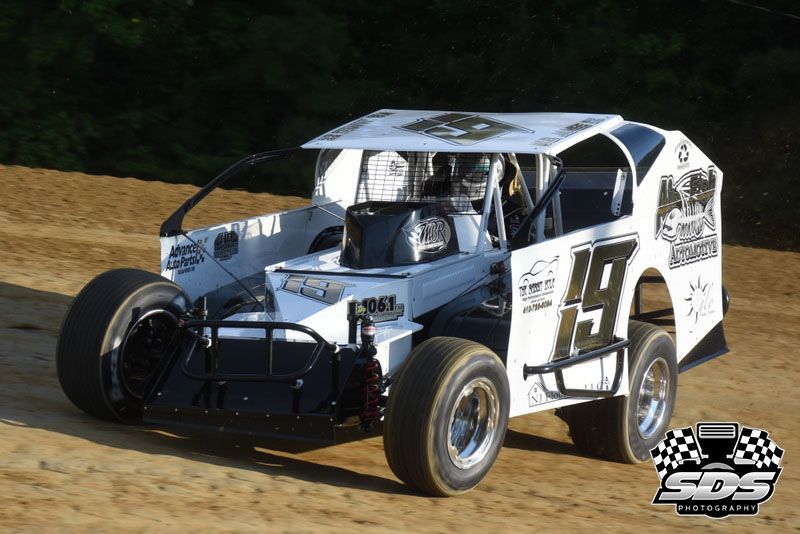 White dirt modified race car, number 19, on a dirt track.