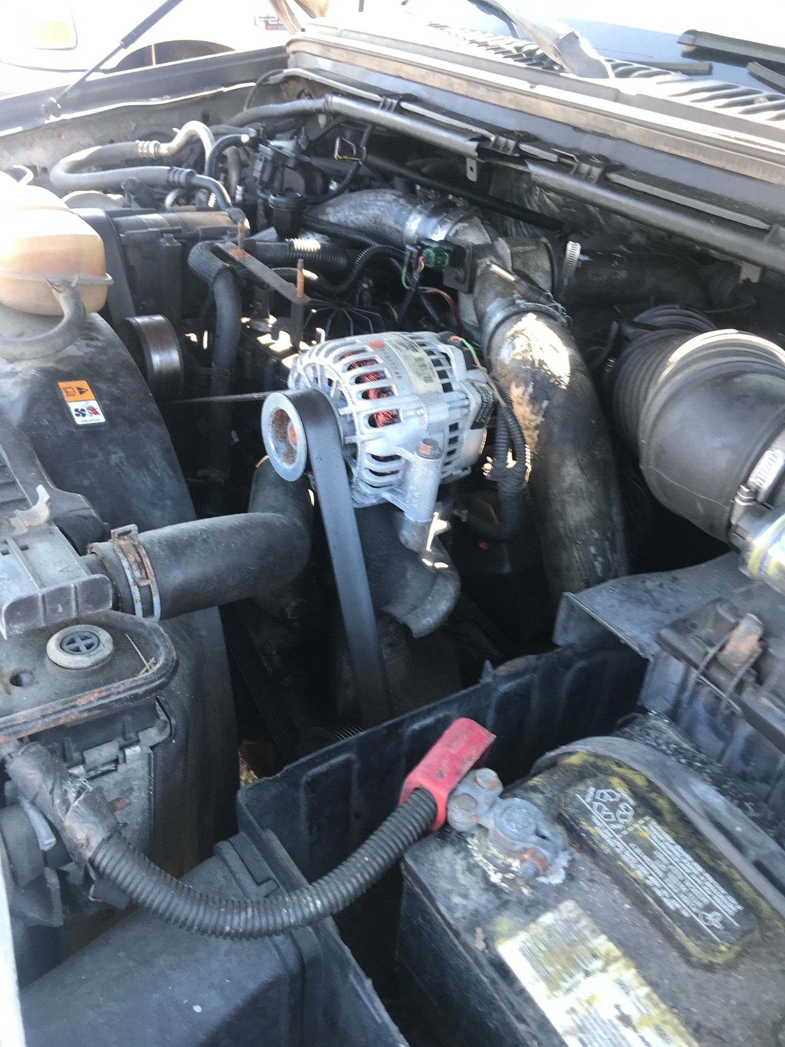 Car engine compartment with alternator, hoses, and battery. Black and grey components.