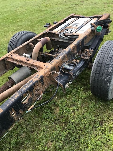 Truck frame on grass with tires, fuel tank, and exhaust components visible.