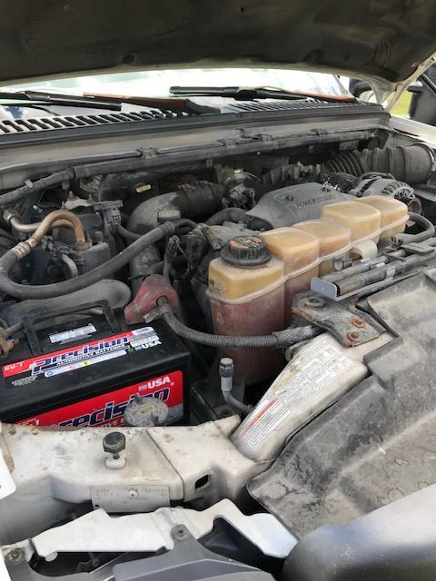 Open truck engine compartment with battery, coolant reservoir, and engine components.