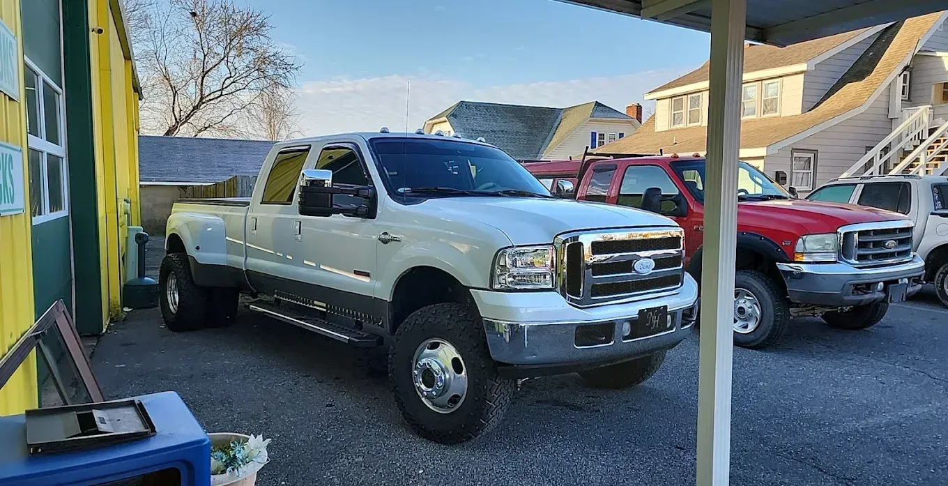 White Ford F-350 dually pickup truck parked next to a red truck, under a building awning on a sunny day.