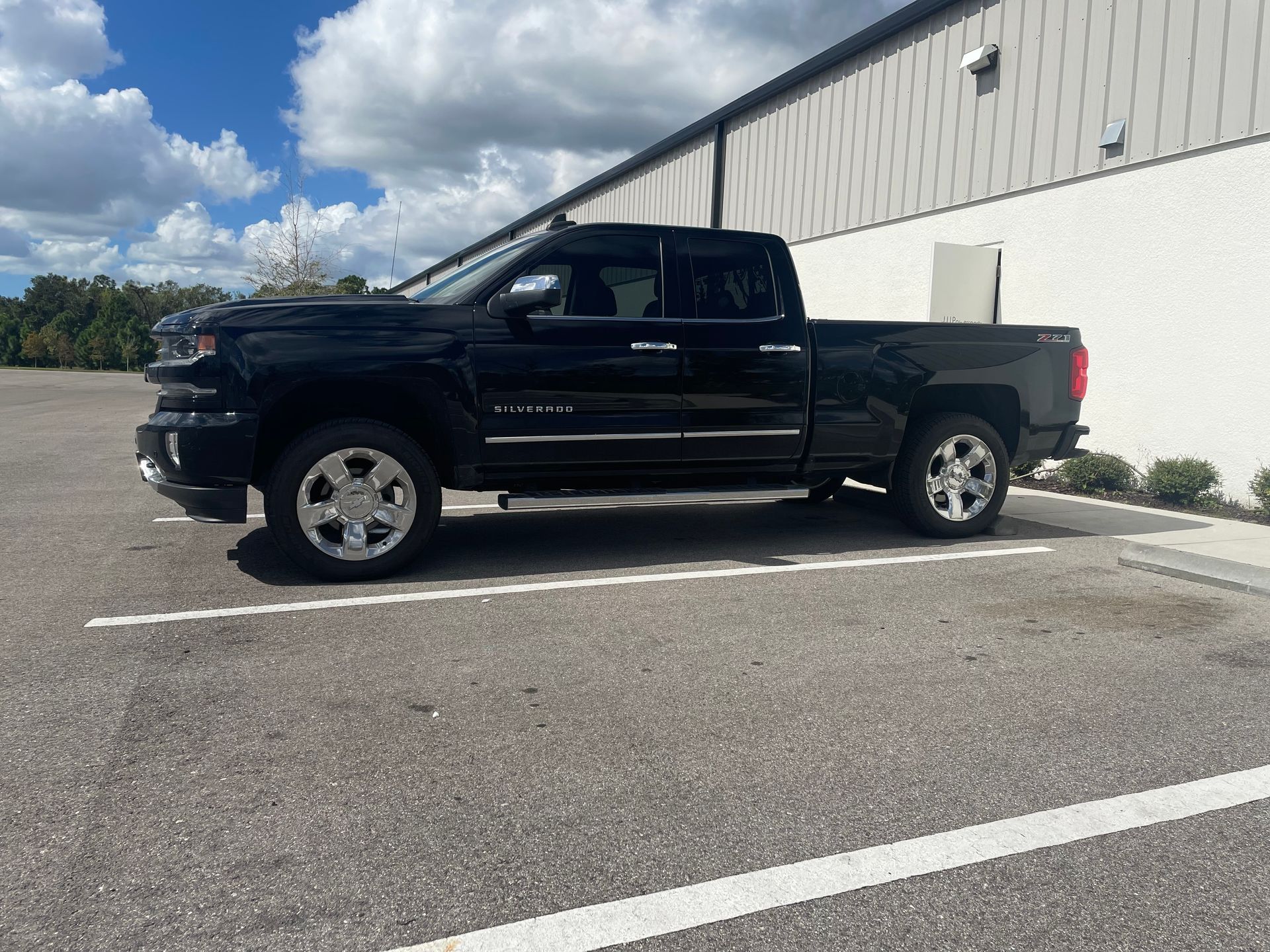 A black truck with chrome wheels and tires is parked in a parking lot.