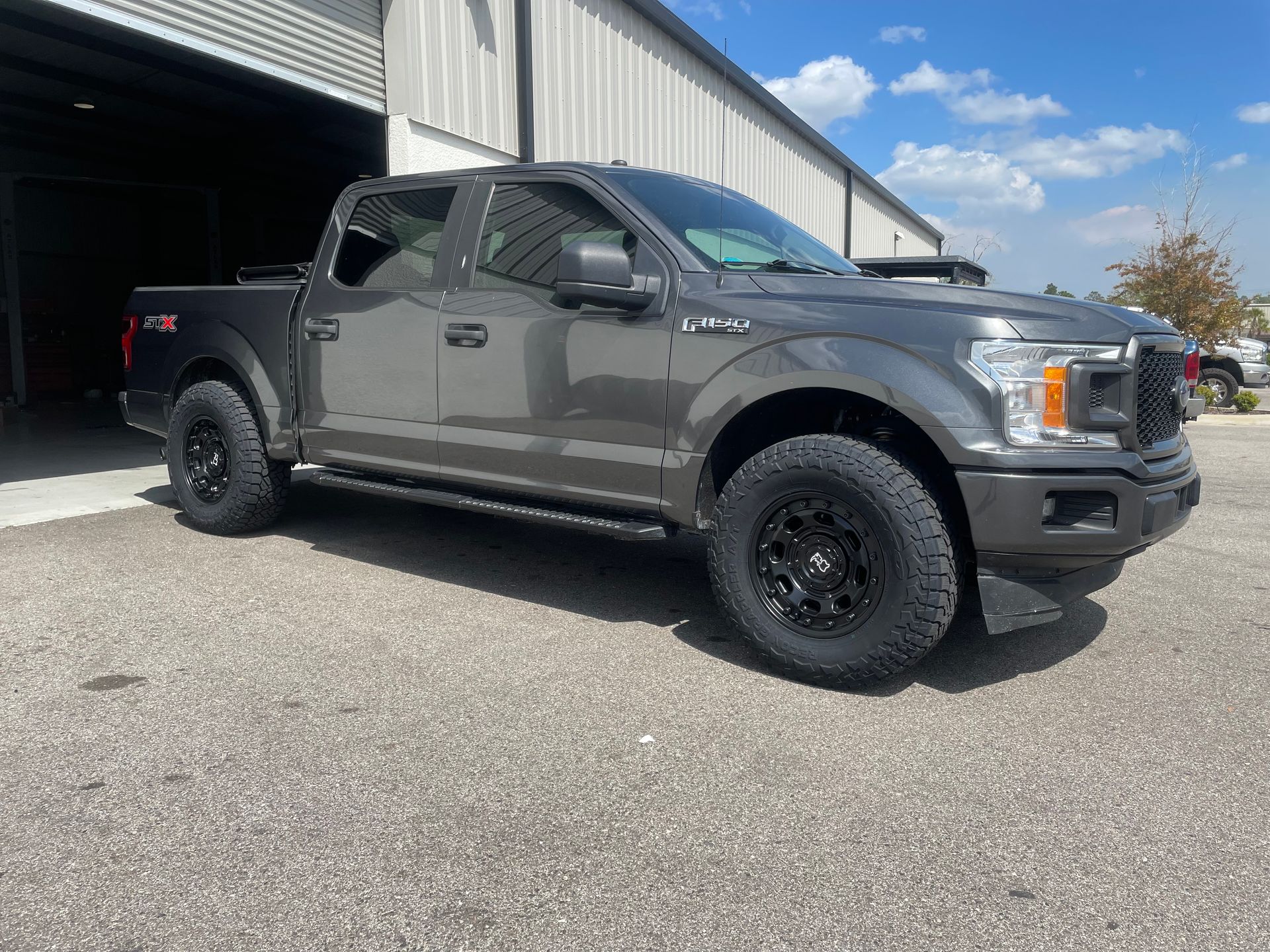 A gray ford f150 truck is parked in front of a garage.