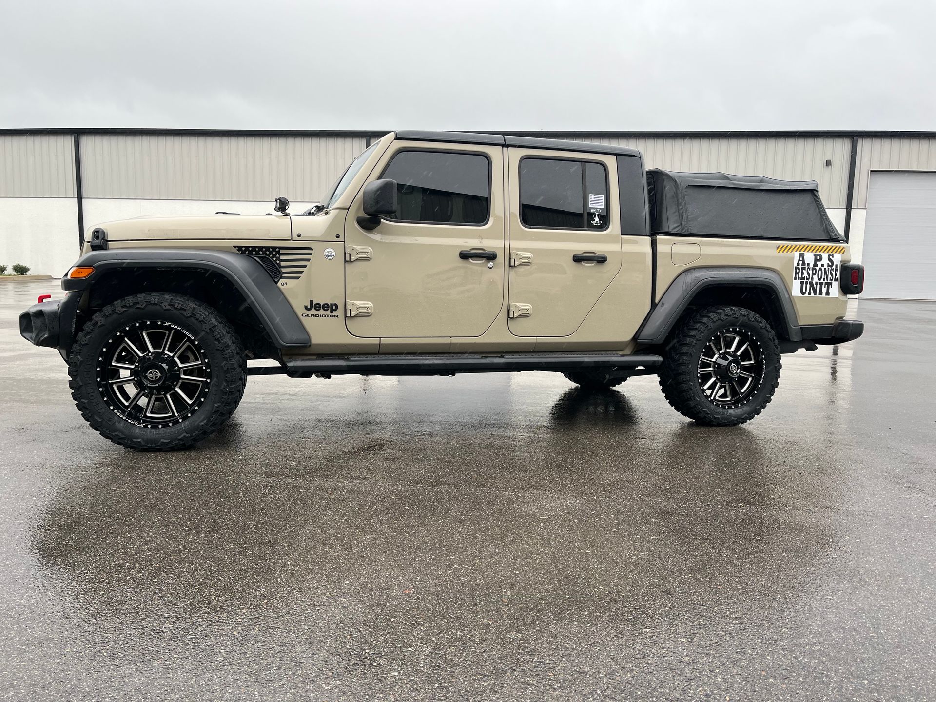 A tan jeep gladiator is parked in a parking lot in front of a building.