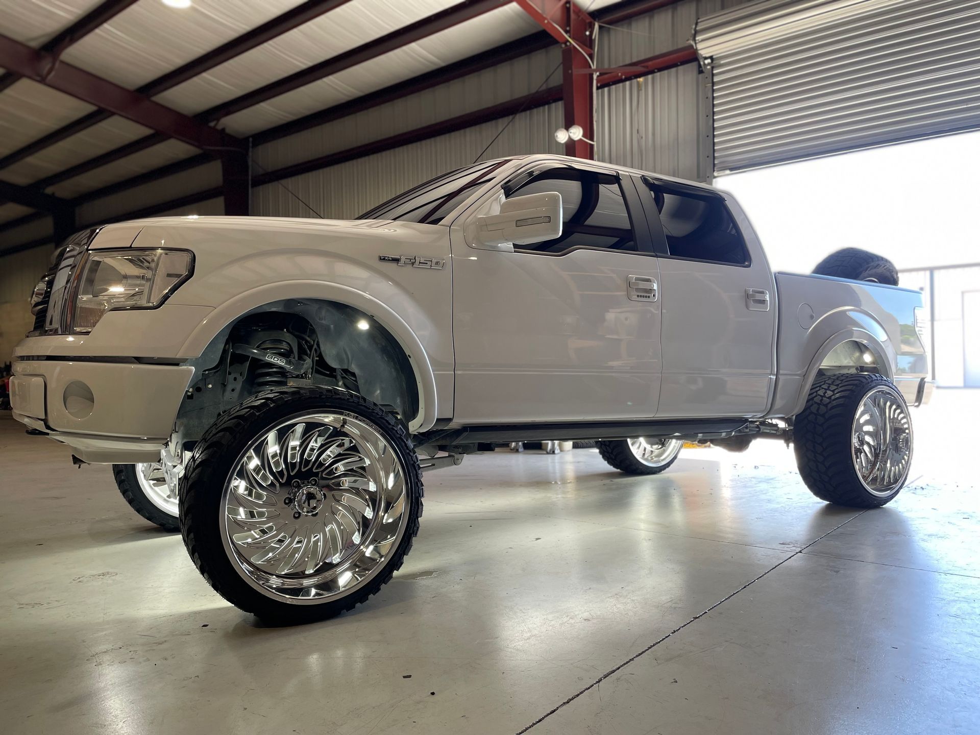 A white truck with chrome wheels is parked in a garage.