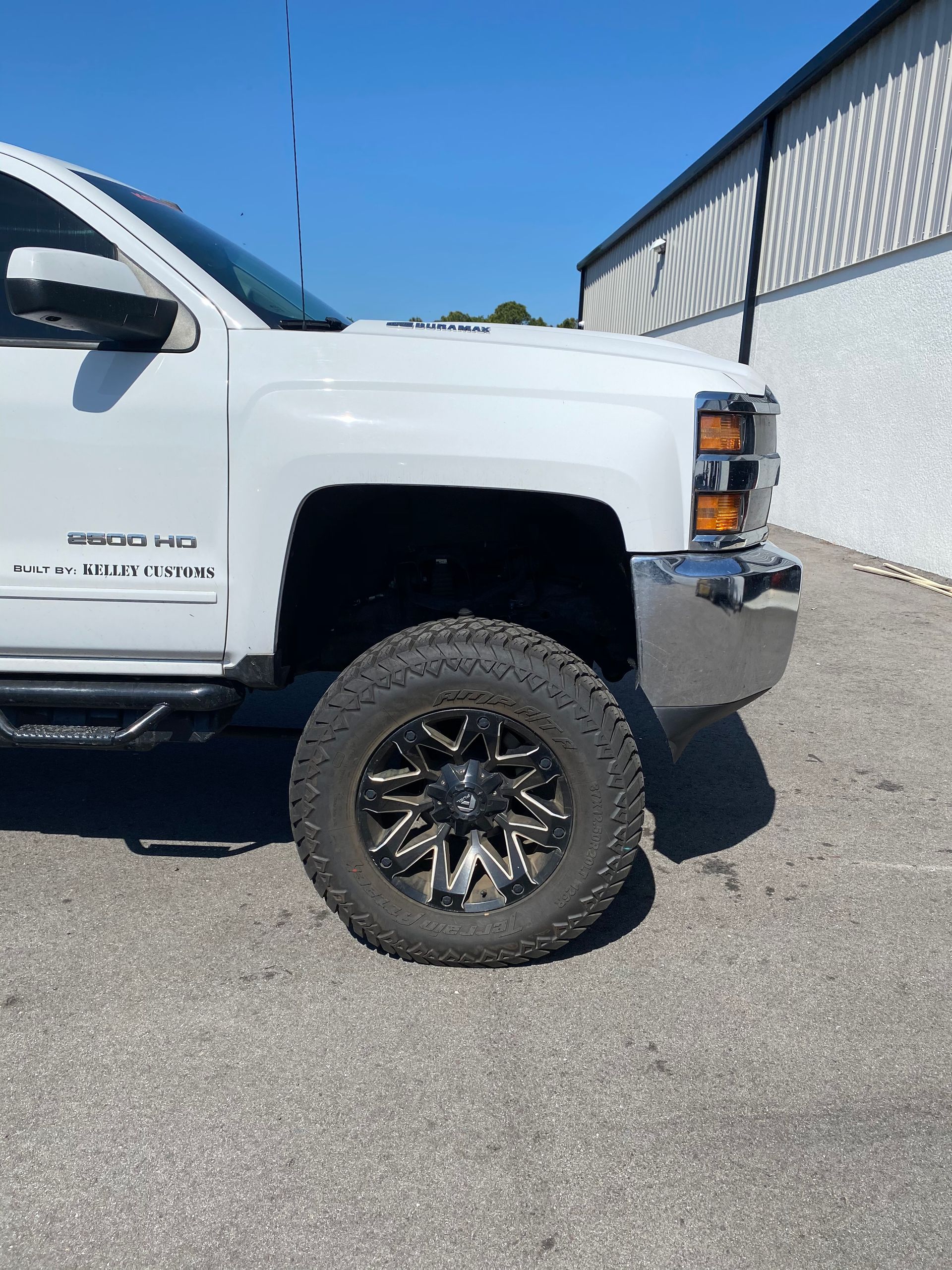 A white truck with black wheels is parked in front of a building.
