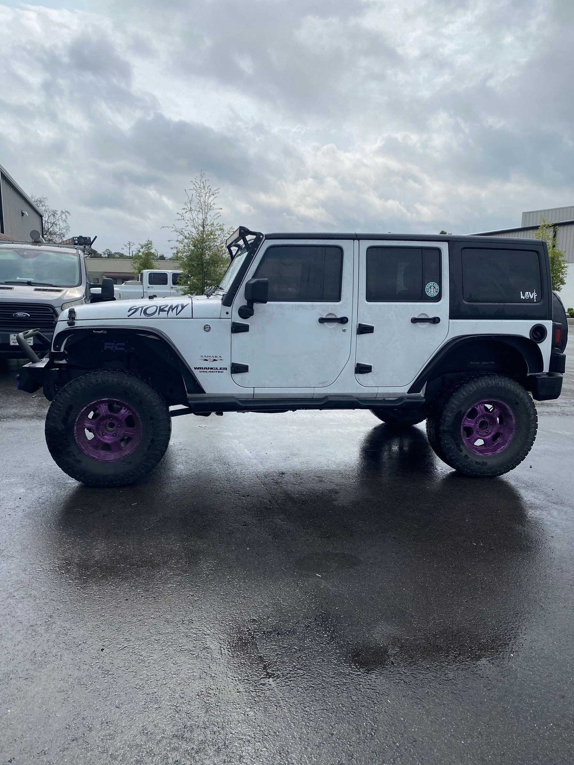 A white jeep with purple wheels is parked in a parking lot.