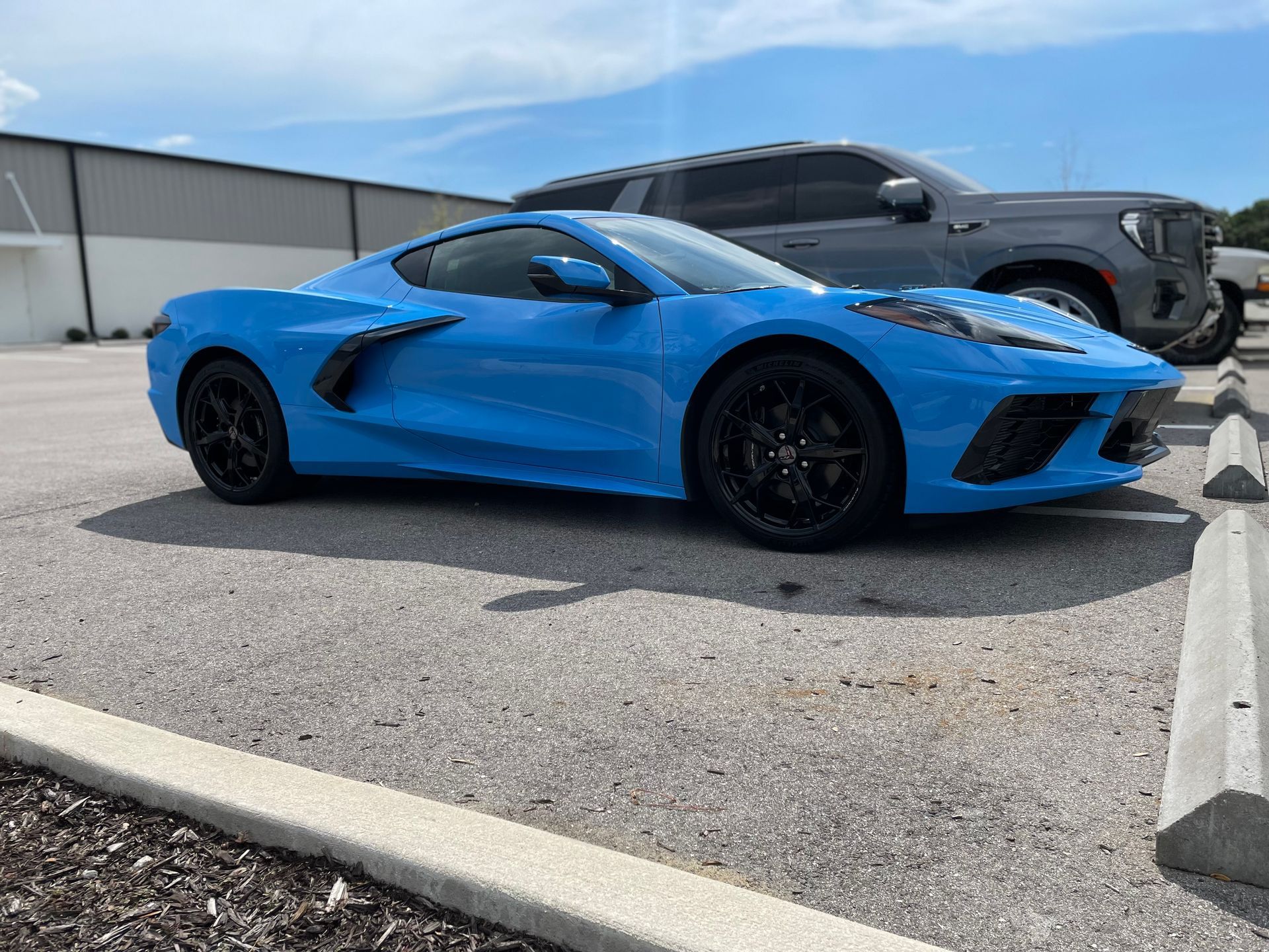 A blue sports car is parked in a parking lot next to a truck.