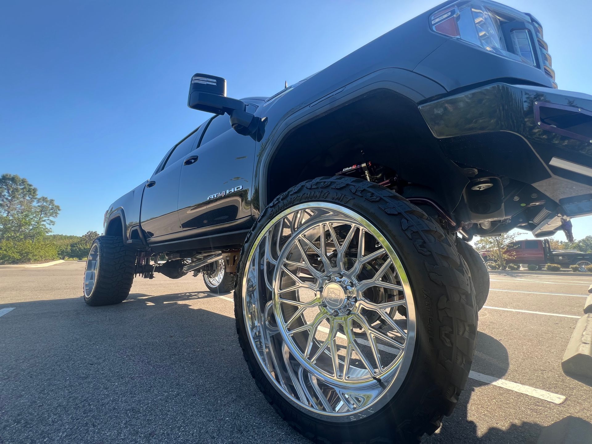 A black truck with a lot of wheels is parked in a parking lot.