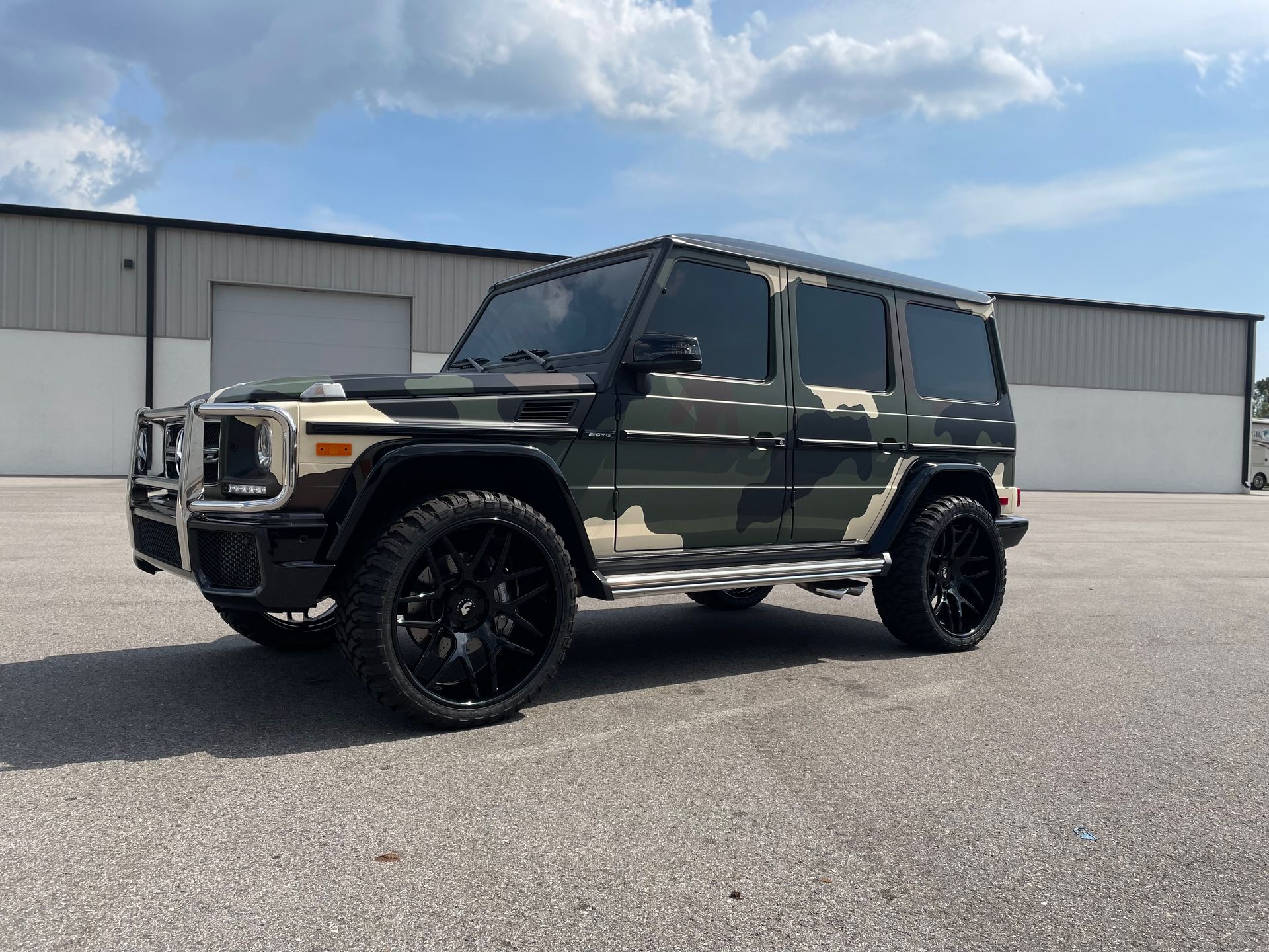 A camouflaged mercedes benz g63 is parked in front of a building.