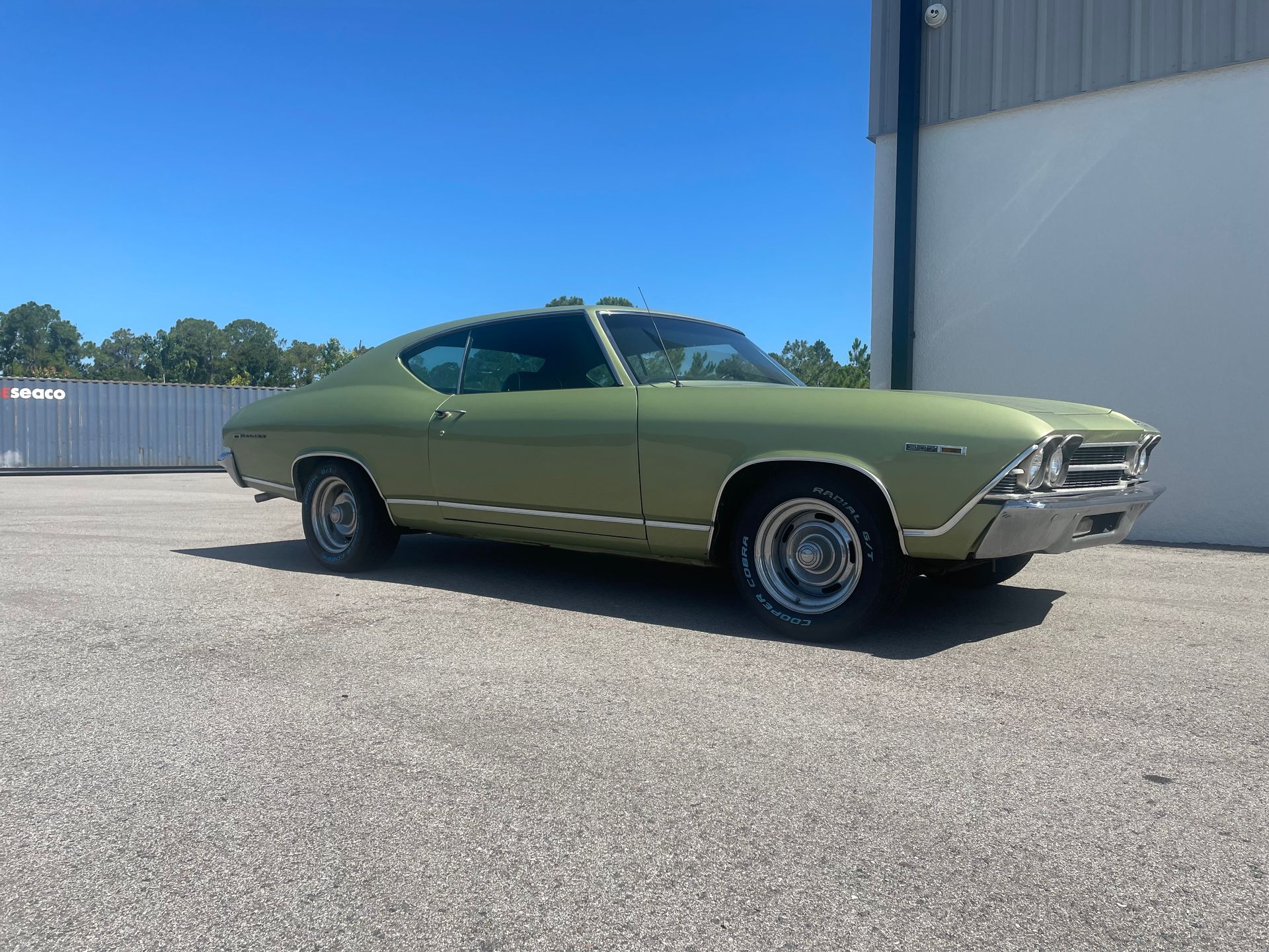 A green car is parked in a parking lot in front of a building.
