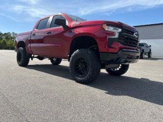 Red Chevrolet Silverado pickup truck with black wheels on a paved surface.