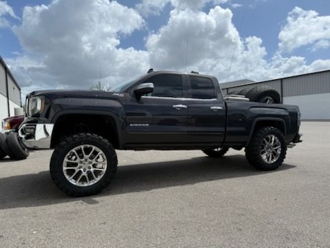 Dark gray lifted truck with chrome wheels parked in front of a building on a sunny day.