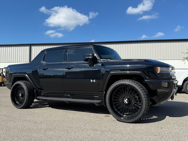 Black Hummer pickup truck with oversized black rims parked outside on a sunny day.