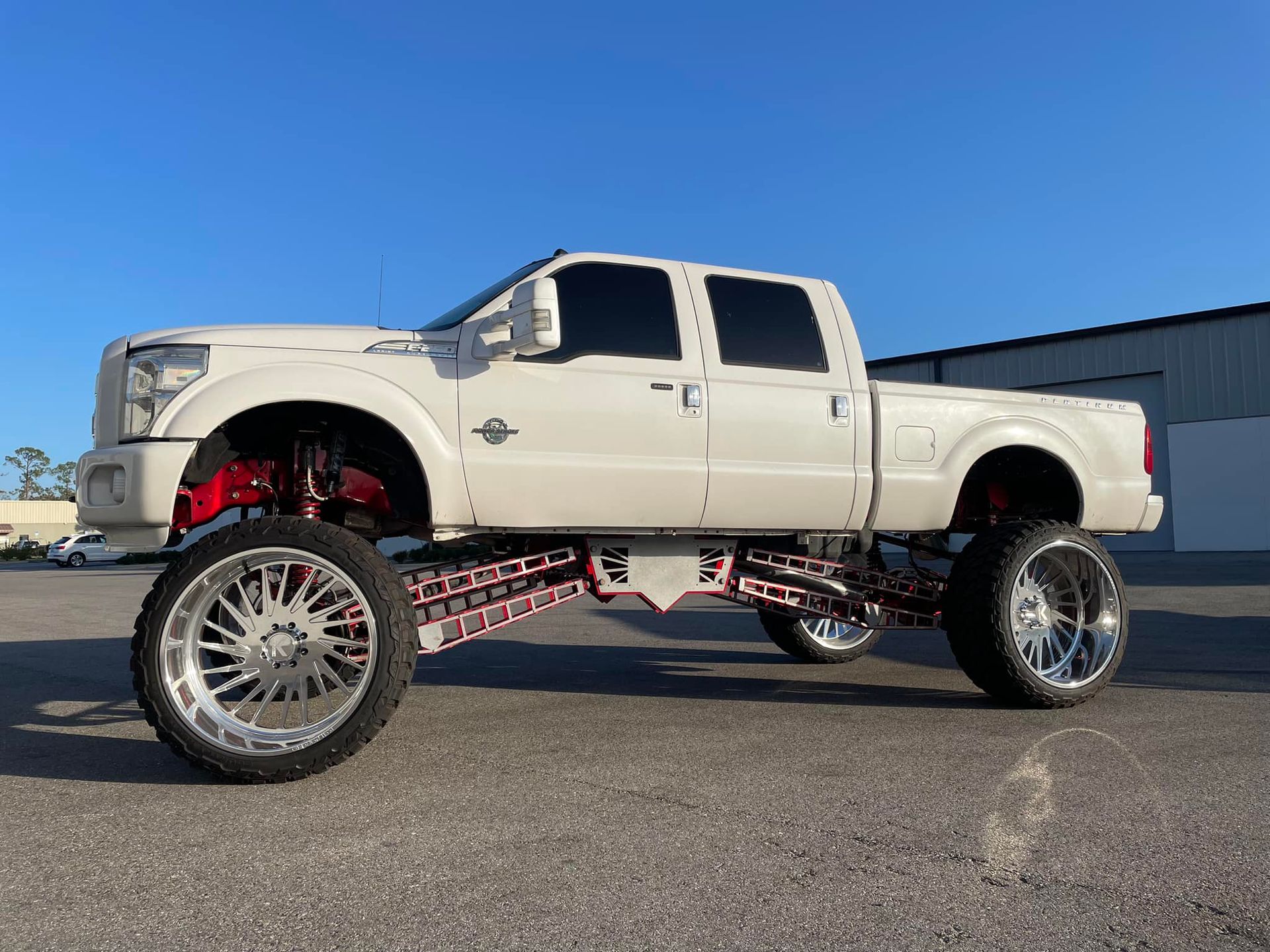A white truck with red wheels is parked in a parking lot.