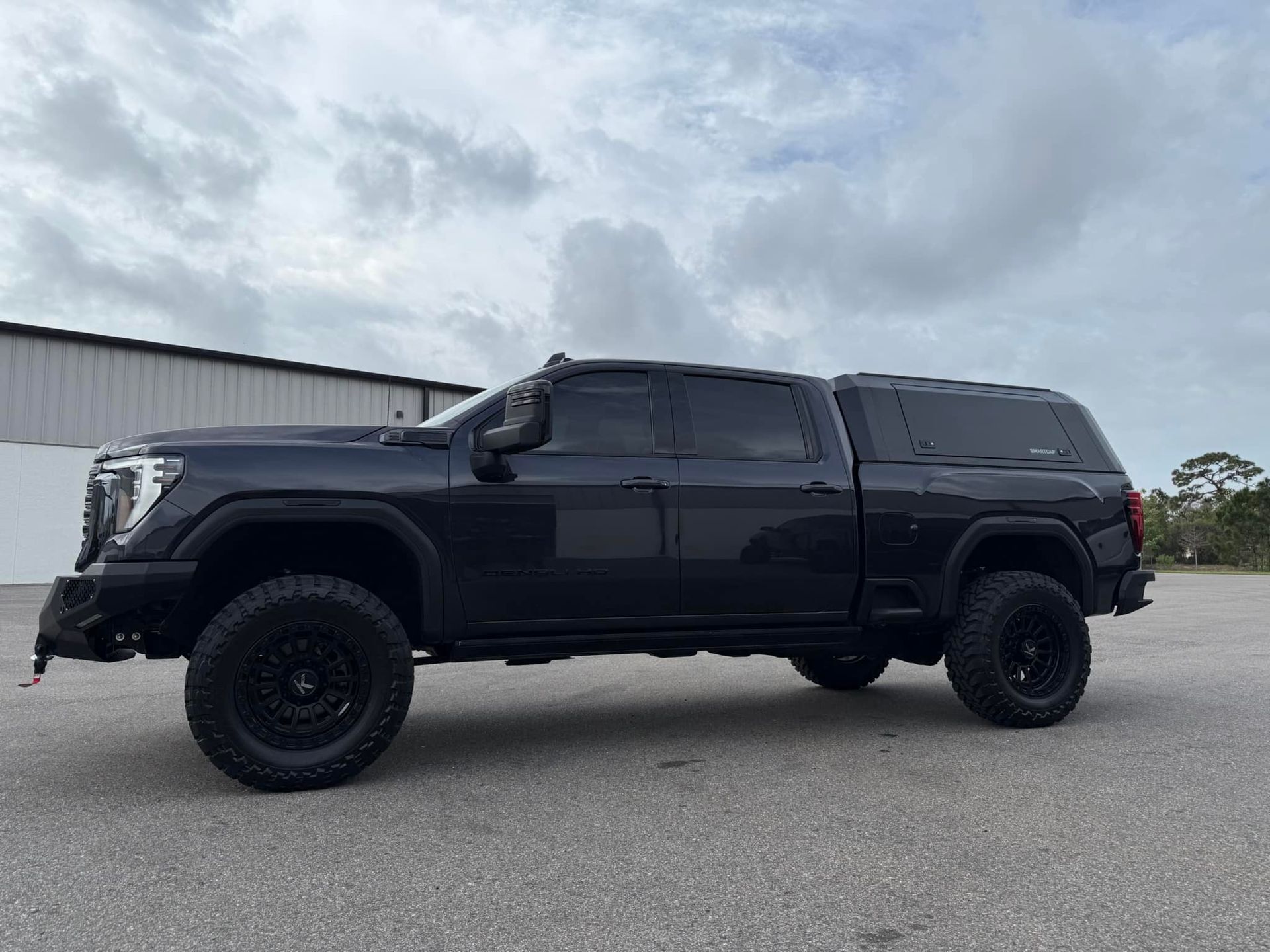 A black truck with a canopy on top of it is parked in a parking lot.