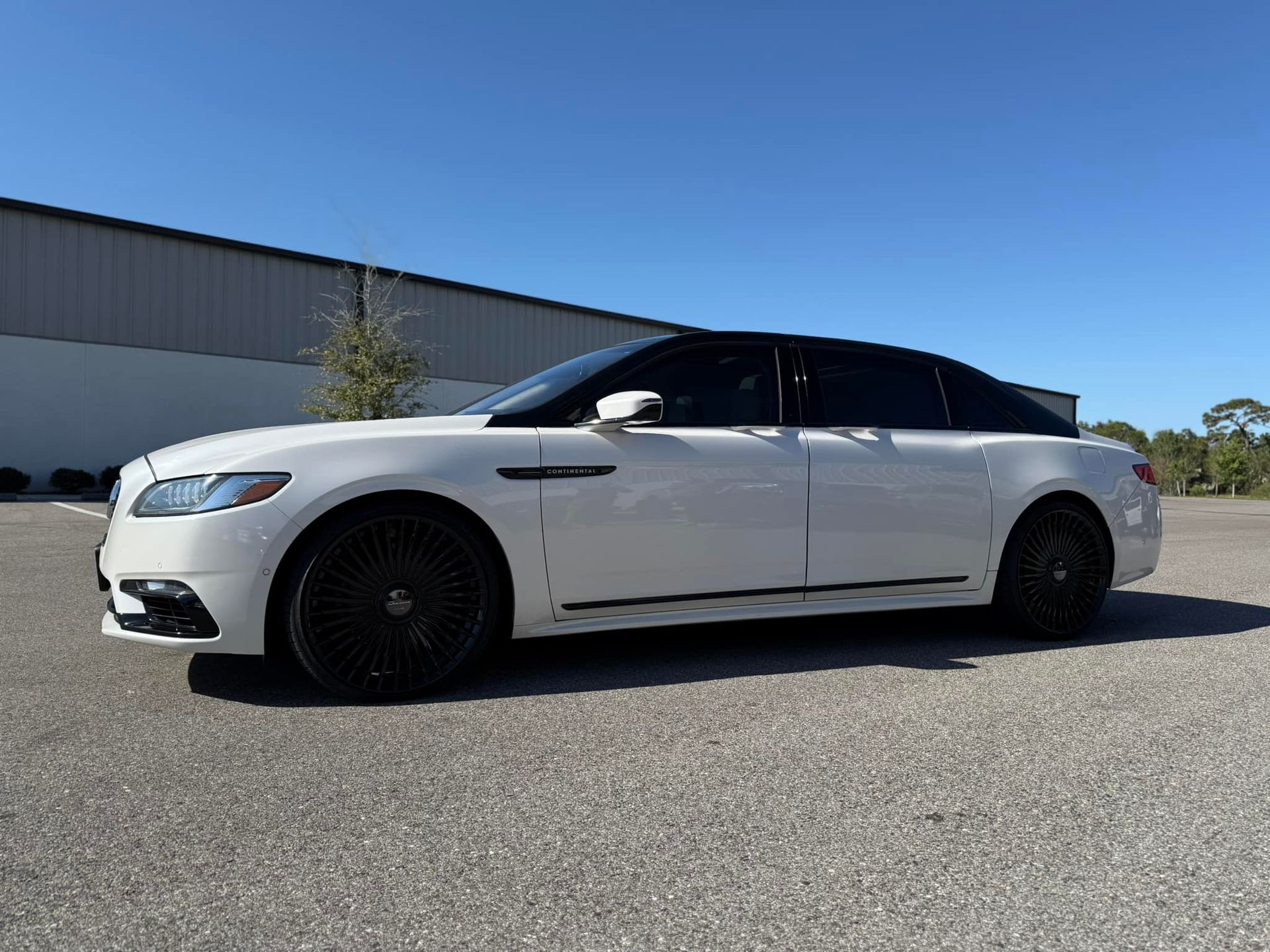 A white limousine is parked in a parking lot in front of a building.