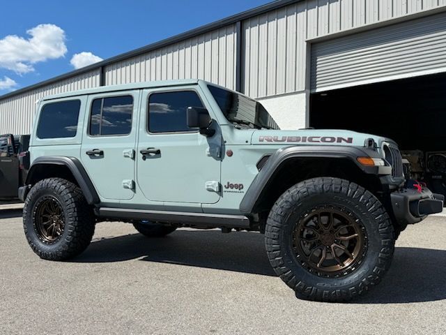 Light green Jeep Rubicon with bronze wheels parked in front of a building.