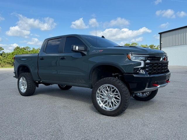 Dark green lifted Chevy Silverado truck with custom chrome wheels on a paved surface.