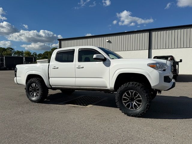 White Toyota Tacoma truck with black wheels parked in front of a building on a sunny day.