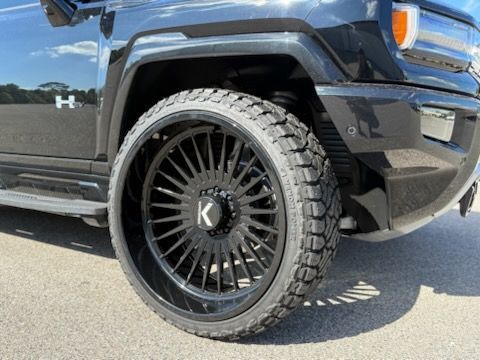Black Hummer EV with large black rims and off road tires, parked on pavement.