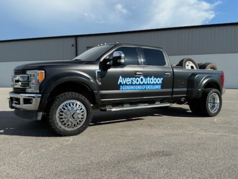 Dark truck with Averso Outdoor logo, spare tires in bed, parked in front of a building.