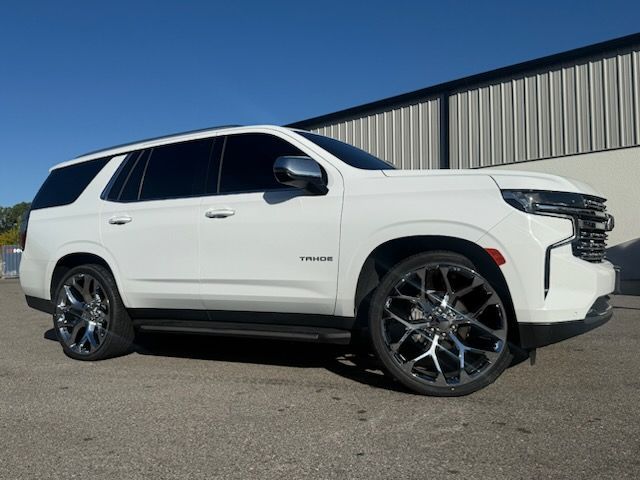 White SUV with large chrome wheels parked outside a building on a sunny day.