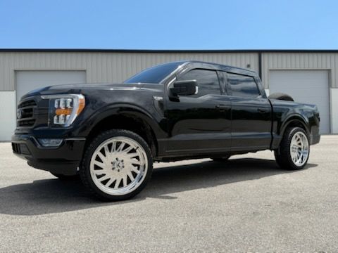 Black Ford F 150 truck with chrome wheels parked in front of a white building on a sunny day.