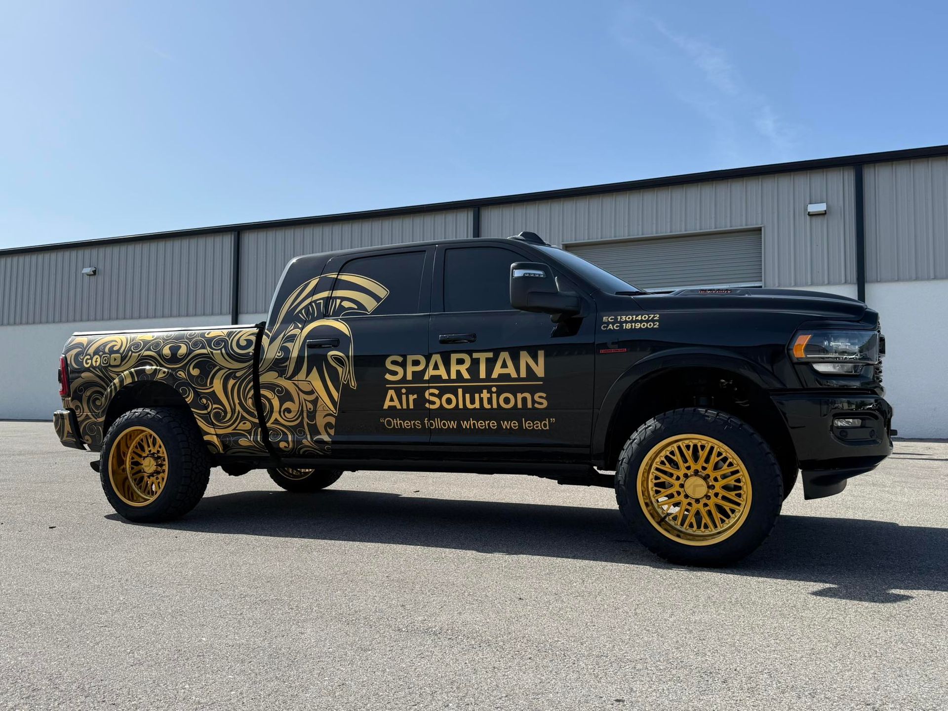 A black and gold spartan air solutions truck is parked in front of a building.