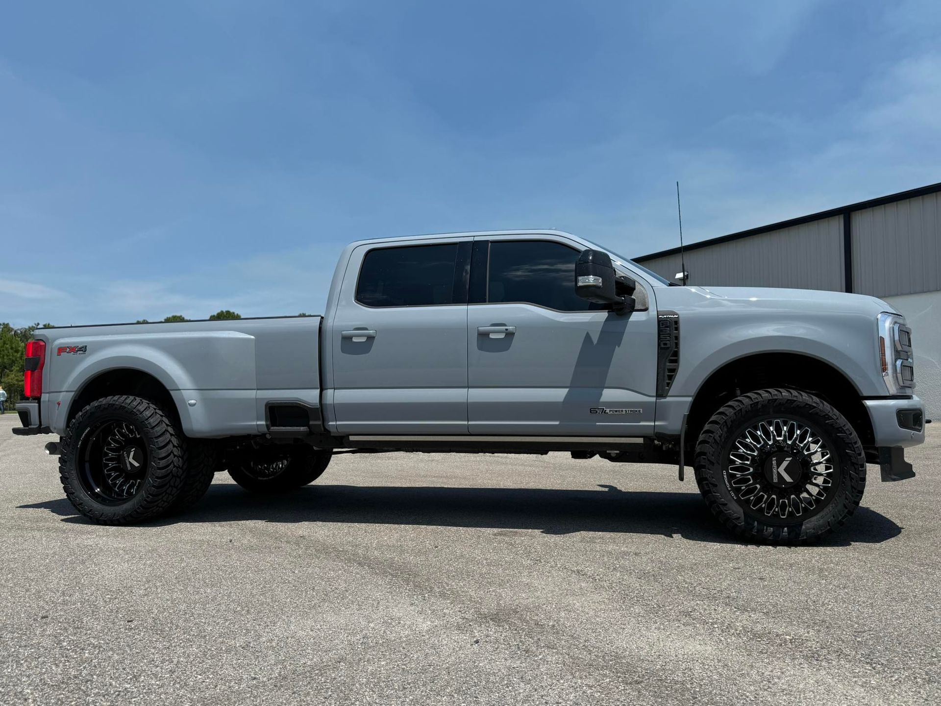 A silver pickup truck is parked on a gravel road in front of a building.