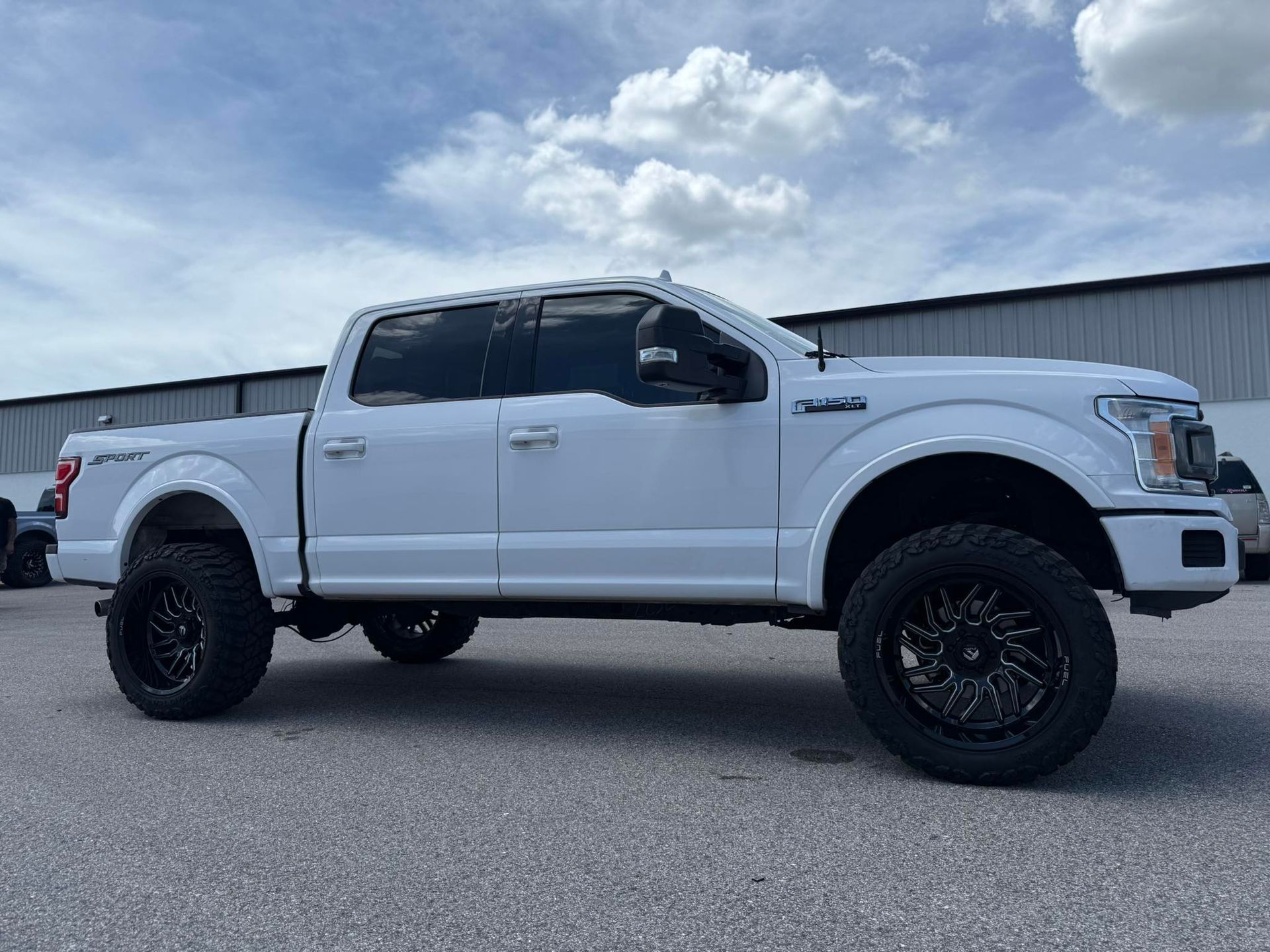 A white pickup truck with black wheels is parked in a parking lot.