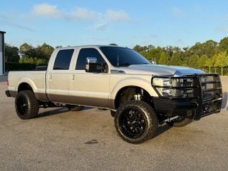 Tan and brown lifted truck with black rims and front bumper guard parked outdoors.