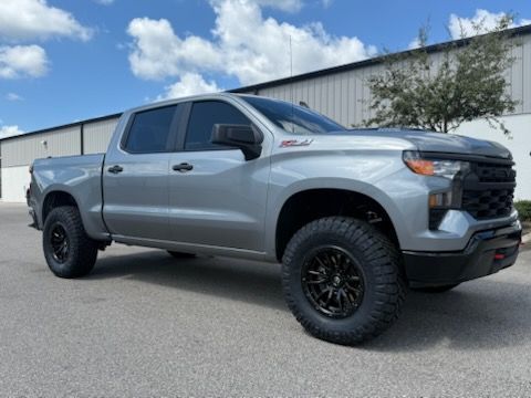 Silver Chevrolet Silverado pickup truck with black wheels, parked on asphalt.