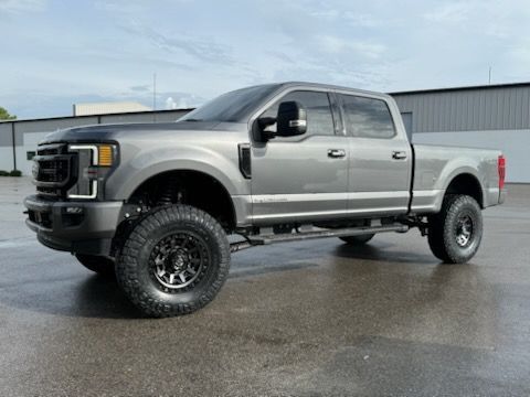 Gray lifted Ford pickup truck with black wheels on a paved surface.