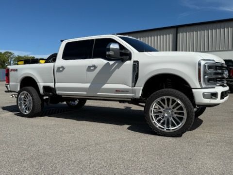 White lifted Ford F 250 truck with chrome wheels parked on asphalt against a building, bright sunny day.