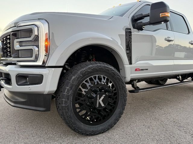 Silver Ford pickup truck with black off road wheels, front quarter view, parked on asphalt.