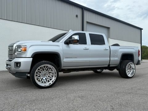 Silver GMC truck with large chrome wheels parked outside a gray building.