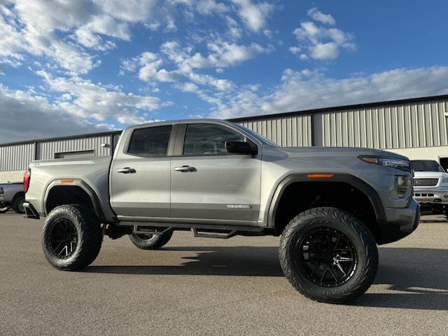 Silver lifted pickup truck with black wheels parked outside a building, blue sky in the background.