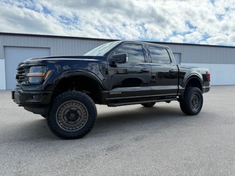 Black Ford pickup truck with off road tires, parked in front of a building with a gray facade.