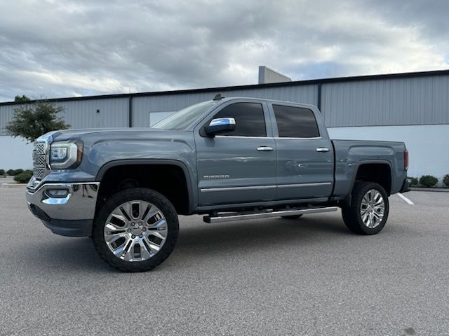 Gray GMC Sierra truck parked in front of a building with chrome wheels and a cloudy sky.