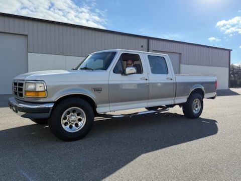 Silver and gray Ford F Series extended cab pickup truck parked in front of a building on a sunny day.