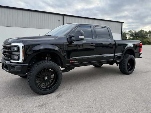 Black lifted Ford truck parked in front of a building black wheels and tires.