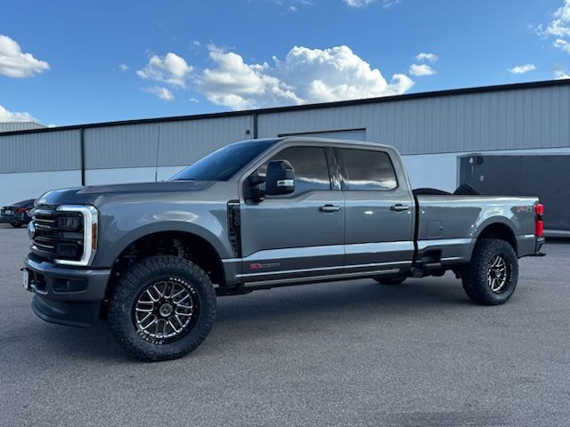 Gray Ford F 350 truck with lifted suspension and custom wheels parked outside a building.