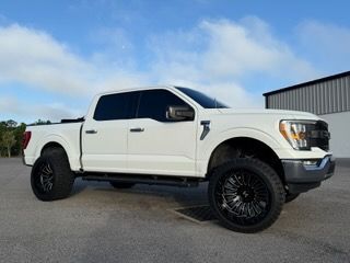 White Ford F 150 truck with black rims and tinted windows parked outside on pavement.