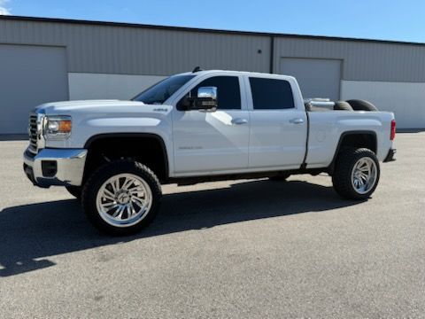 White lifted truck with chrome wheels parked in front of a gray building on a sunny day.