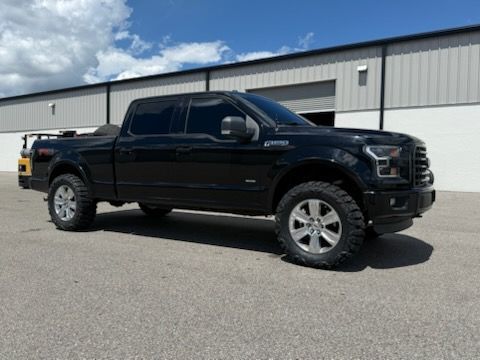 Black Ford F 150 truck with tinted windows, parked on pavement in front of a building under a partly cloudy sky.
